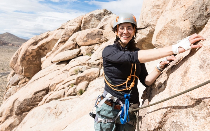 a student in rock climbing gear smiles at the camera amongst tan rocks